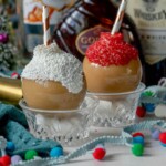 chocolate caramel whiskey cocktails in a plastic ornament with white chocolate and sprinkles and a straw inside in front of christmas decor
