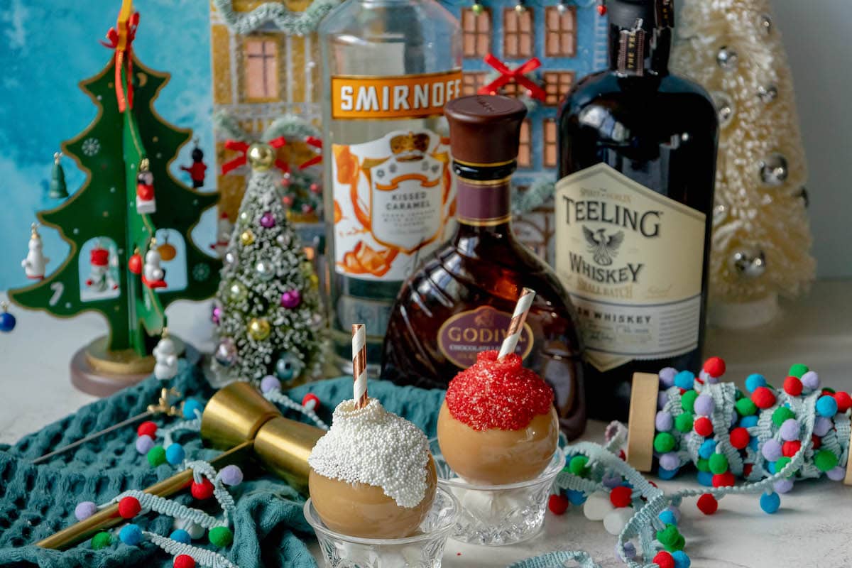 chocolate caramel whiskey cocktails in a plastic ornament with white chocolate and sprinkles and a straw inside in front of christmas decor