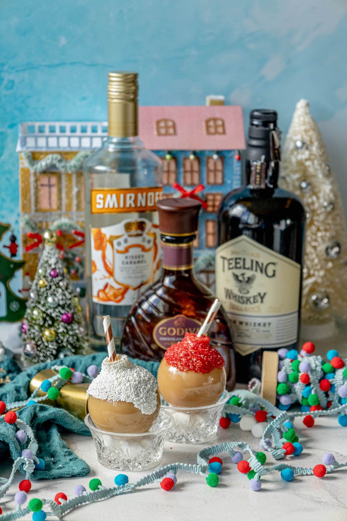 chocolate caramel whiskey cocktails in a plastic ornament with white chocolate and sprinkles and a straw inside in front of christmas decor