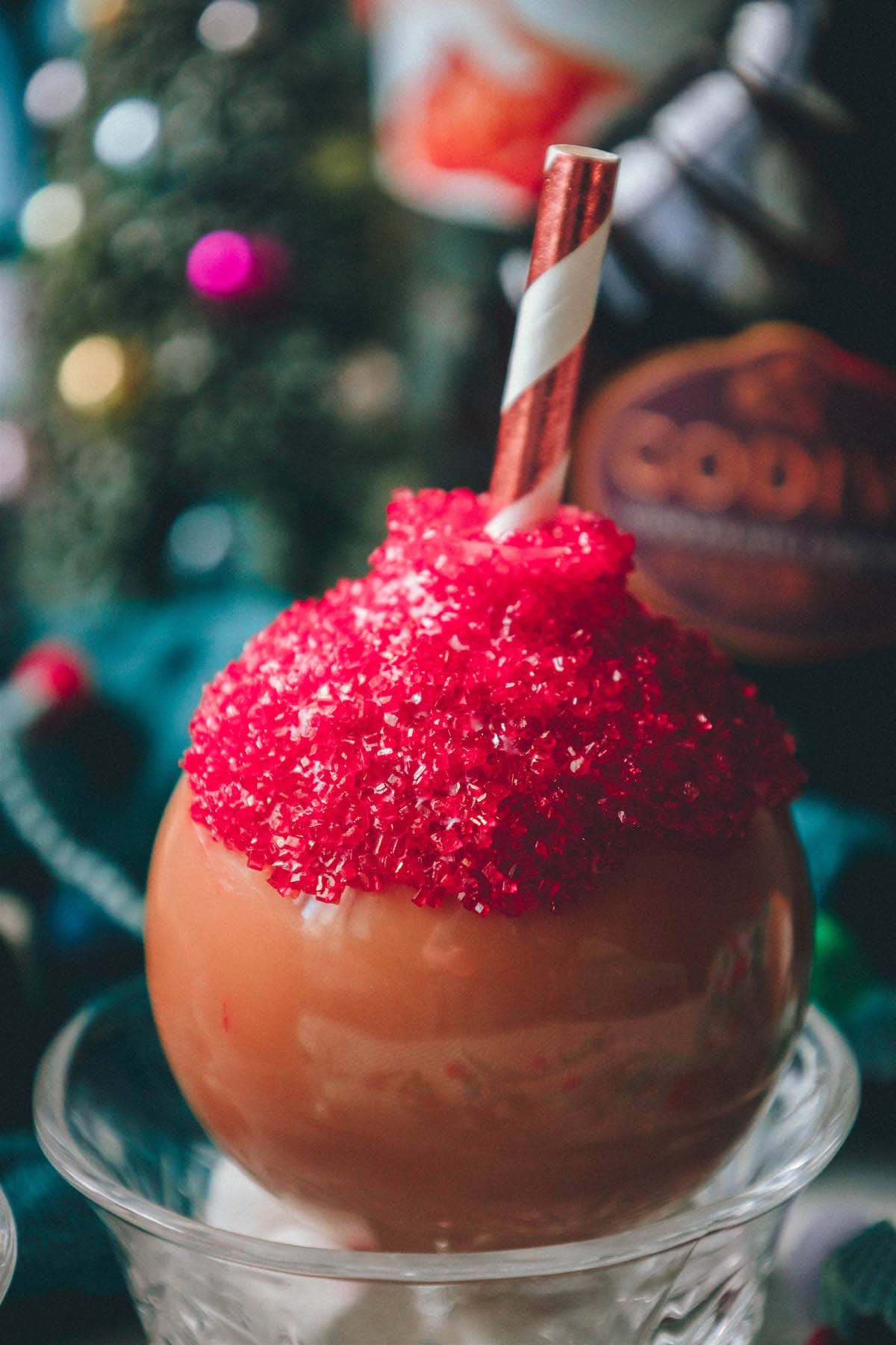chocolate caramel whiskey cocktail in a plastic ornament with white chocolate and red sanding sugar and a straw inside in front of christmas decor
