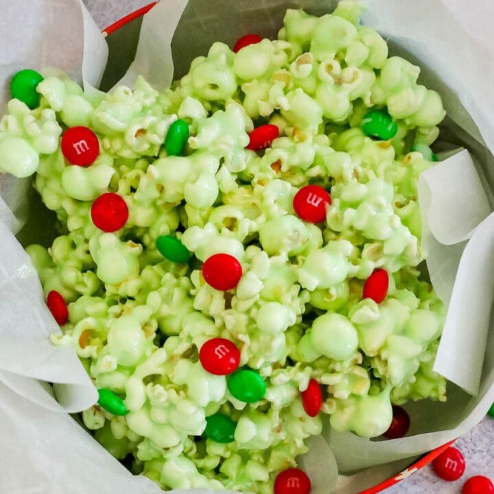 green candy coated popcorn with green and red christmas candies in a bowl on a table