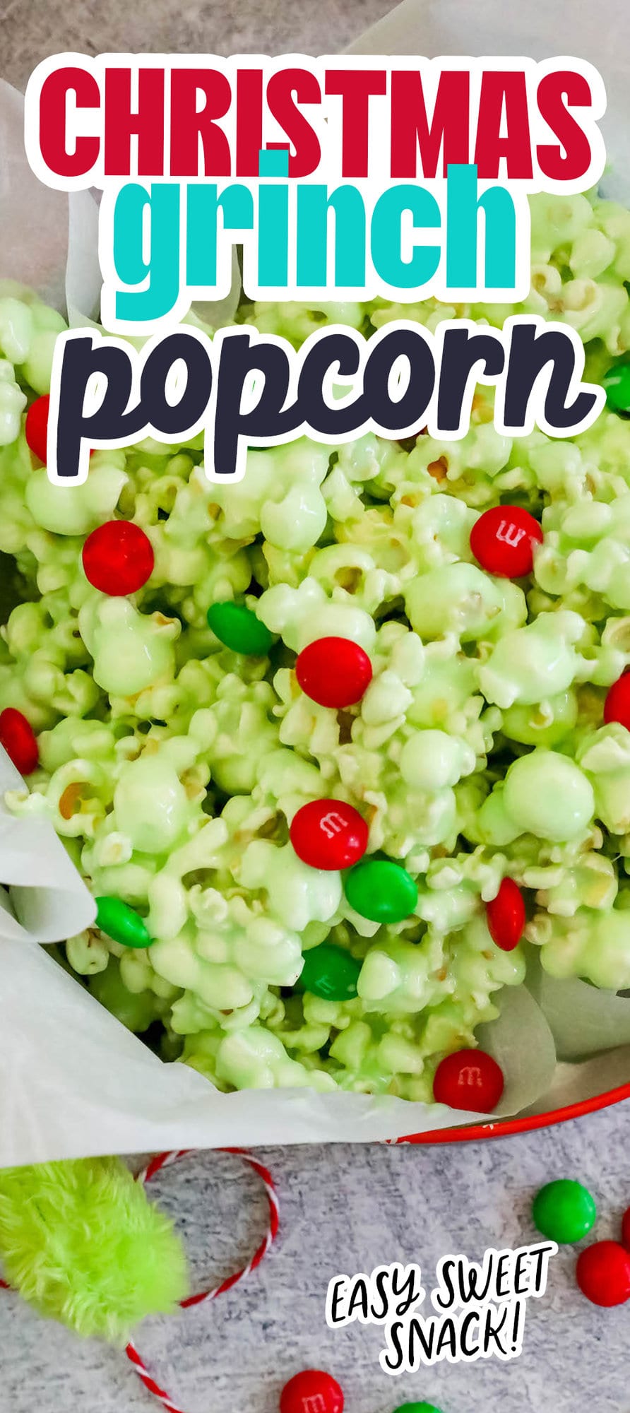 green candy coated popcorn with green and red christmas candies in a bowl on a table with ribbon 