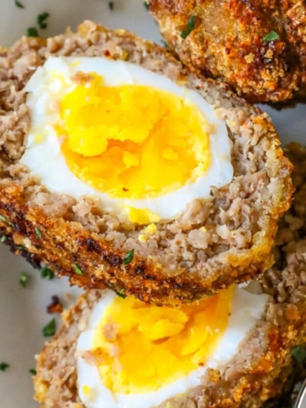 scotch eggs with keto pork rind crust cut in half on a white plate