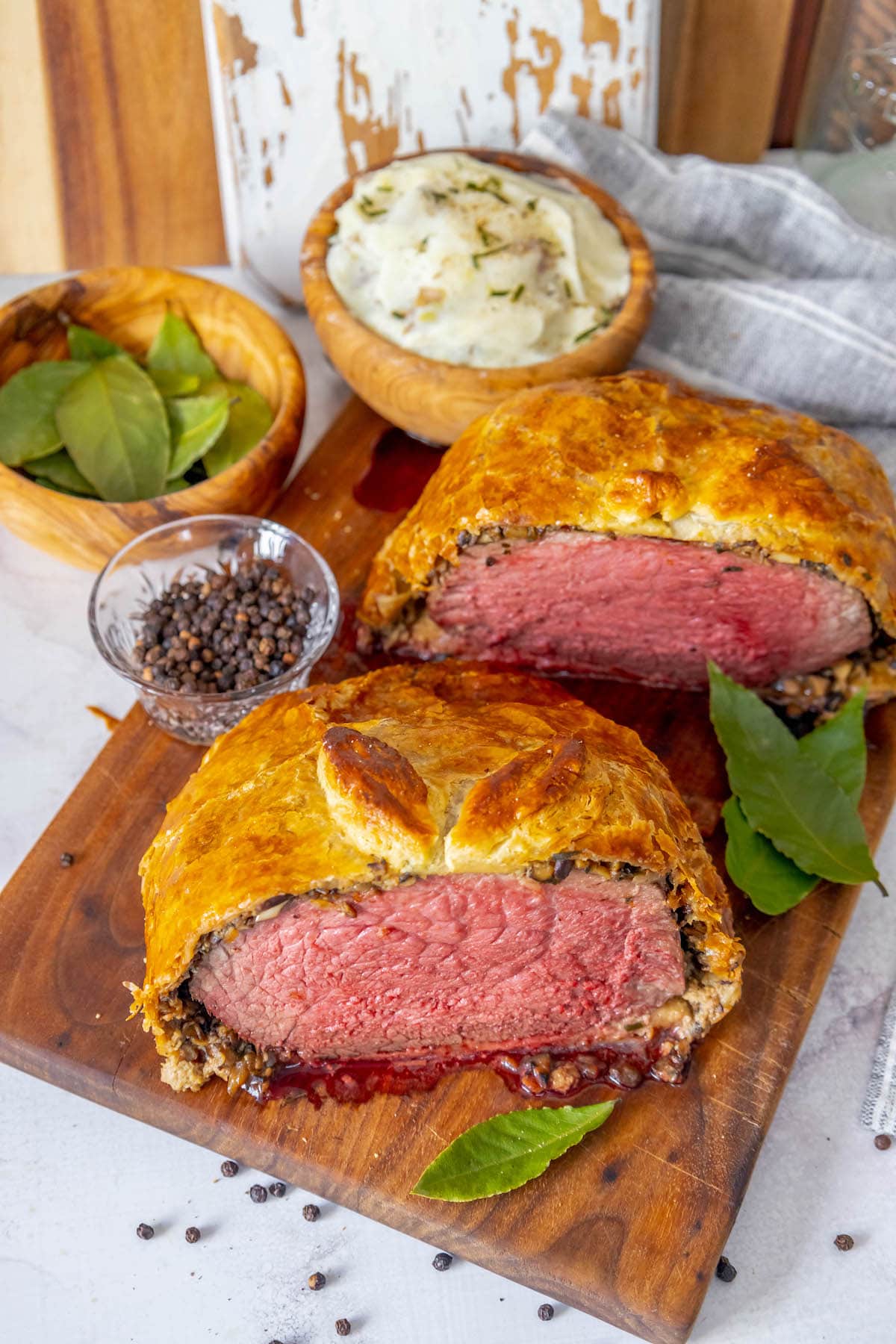 beef wellington wrapped in puff pastry sliced in half sitting on a cutting board with bay leaves