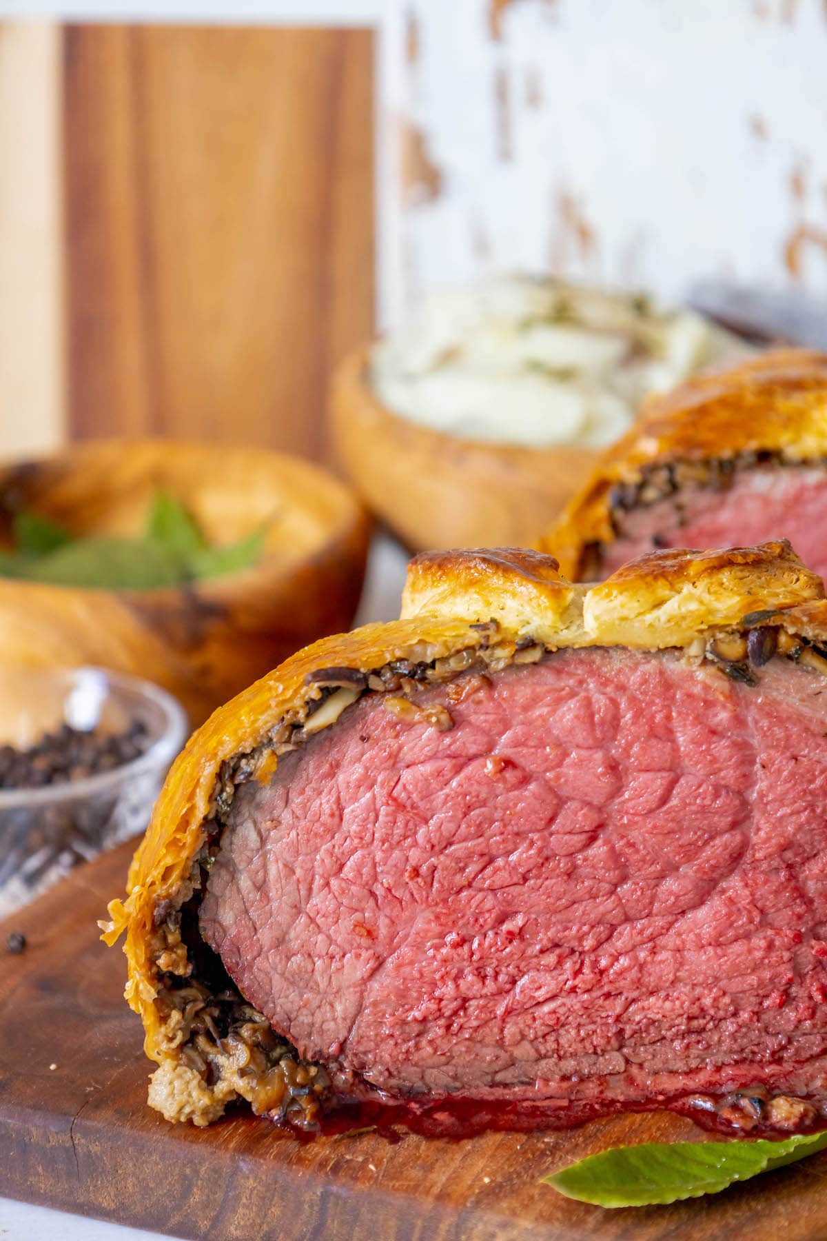 beef wellington wrapped in puff pastry sliced in half sitting on a cutting board with bay leaves