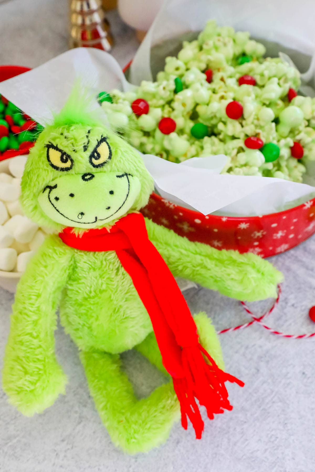 a grinch doll in front of a red bowl with christmas candied popcorn colored green with green and red candy