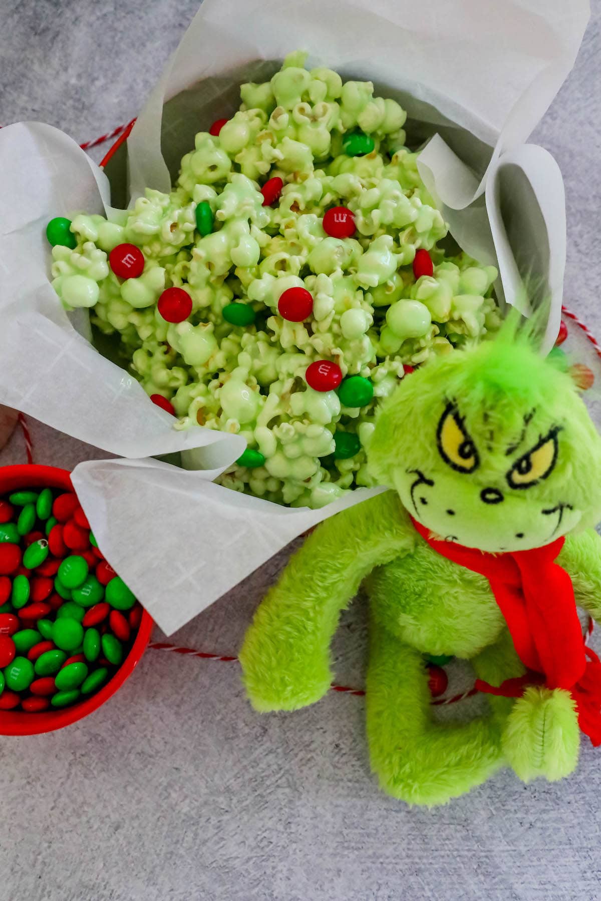 christmas candy popcorn in a bowl on a table nest to a bowl of m&ms and a grinch doll 