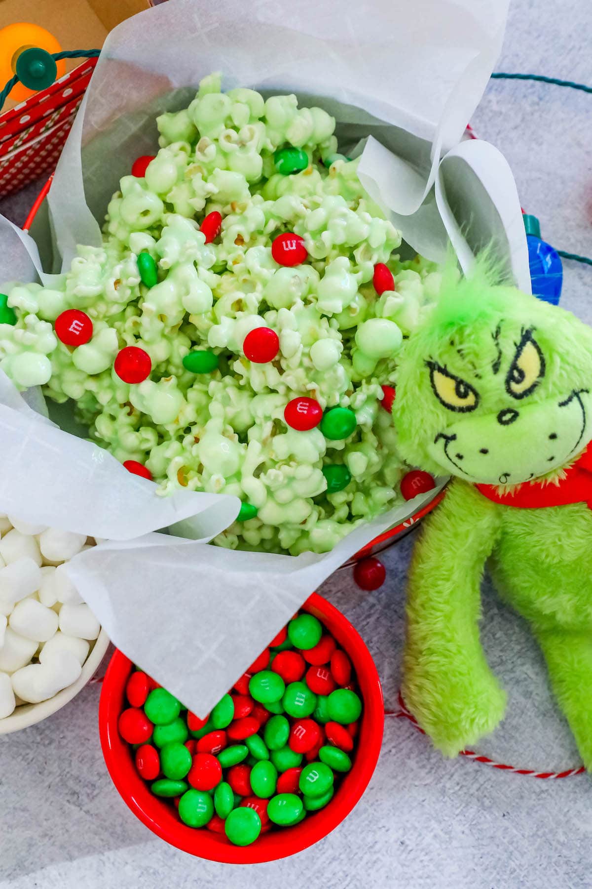 christmas candy popcorn in a bowl on a table nest to a bowl of m&ms and a grinch doll 