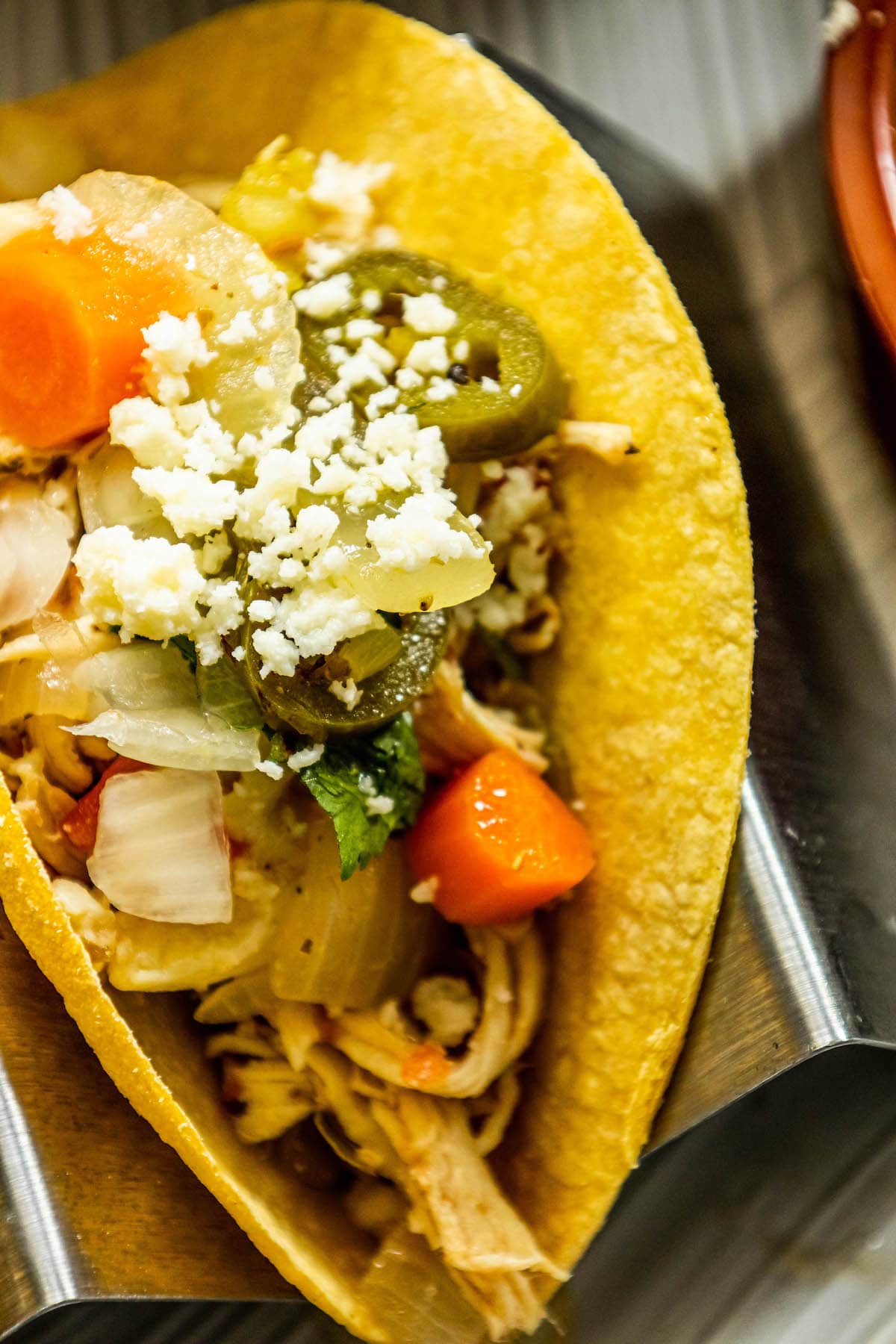 a taco in a stand with shredded chicken and pickled carrots and jalapenos piled on top 