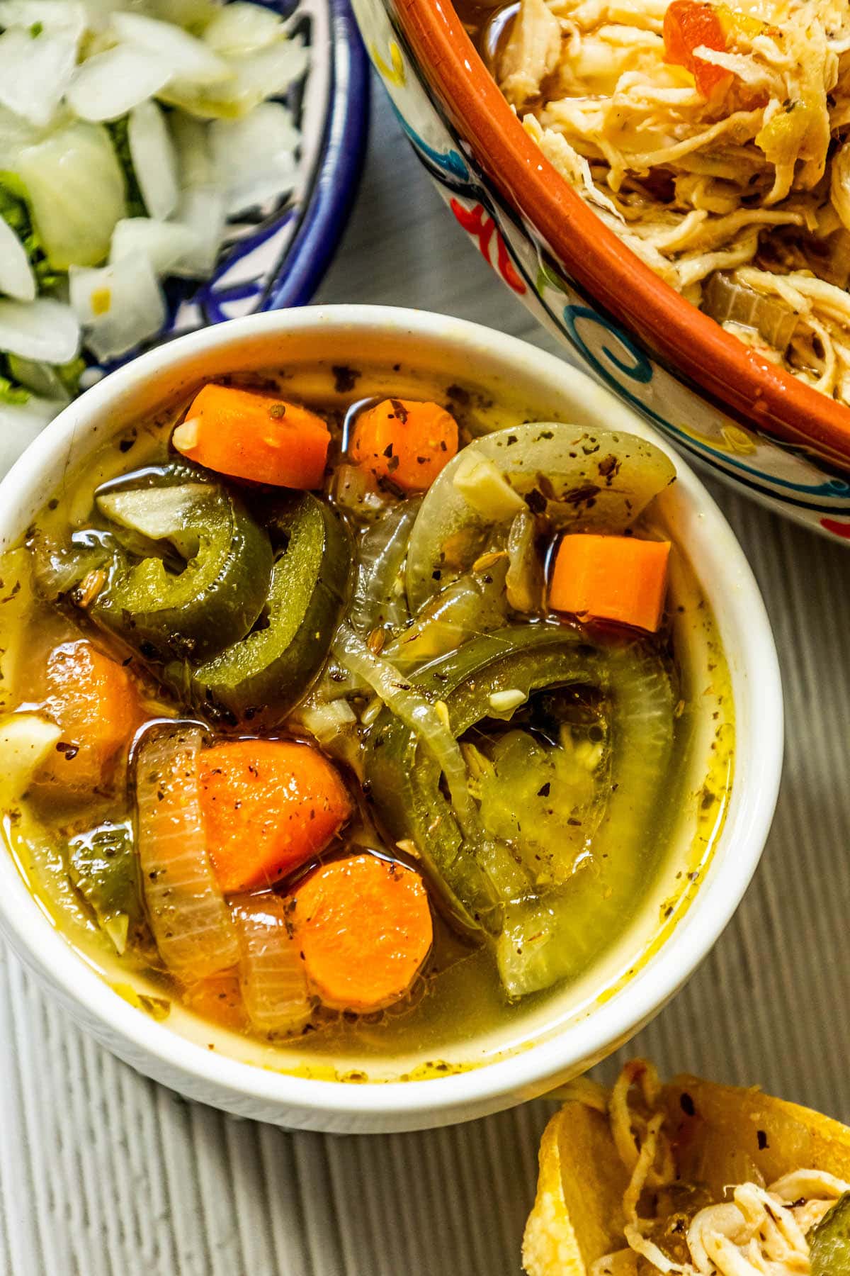 pickled carrots, onions, and jalapeno salsa in a white bowl on a table next to a bowl of chopped onions and a bowl of shredded chicken