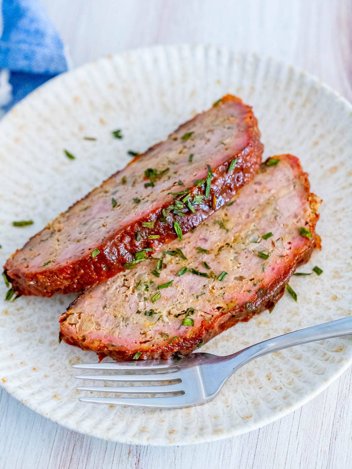 two slices of smoked meatloaf on a white plate with basil garnish
