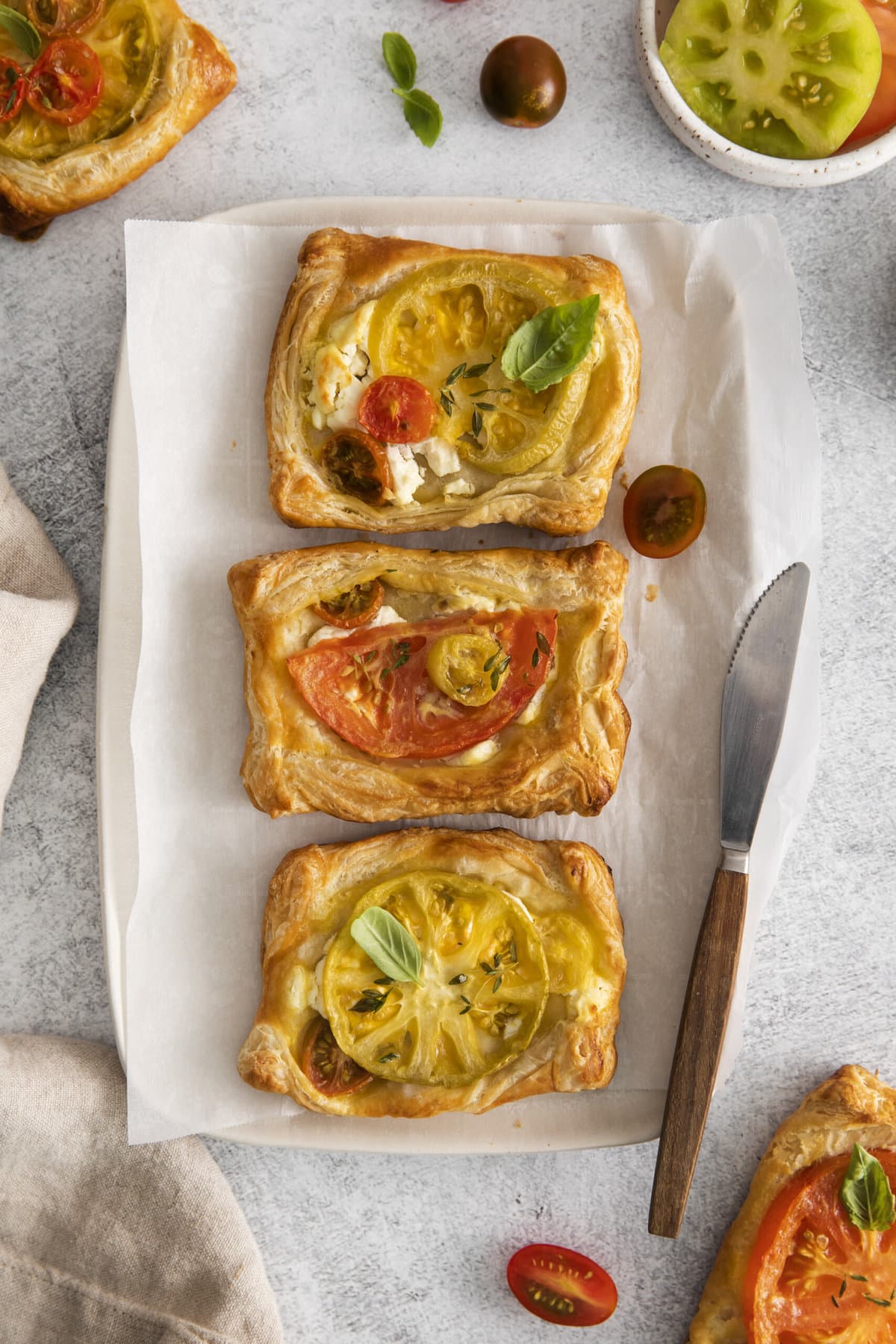 three tomato goat cheese tarts in a row with a knife next to it. 