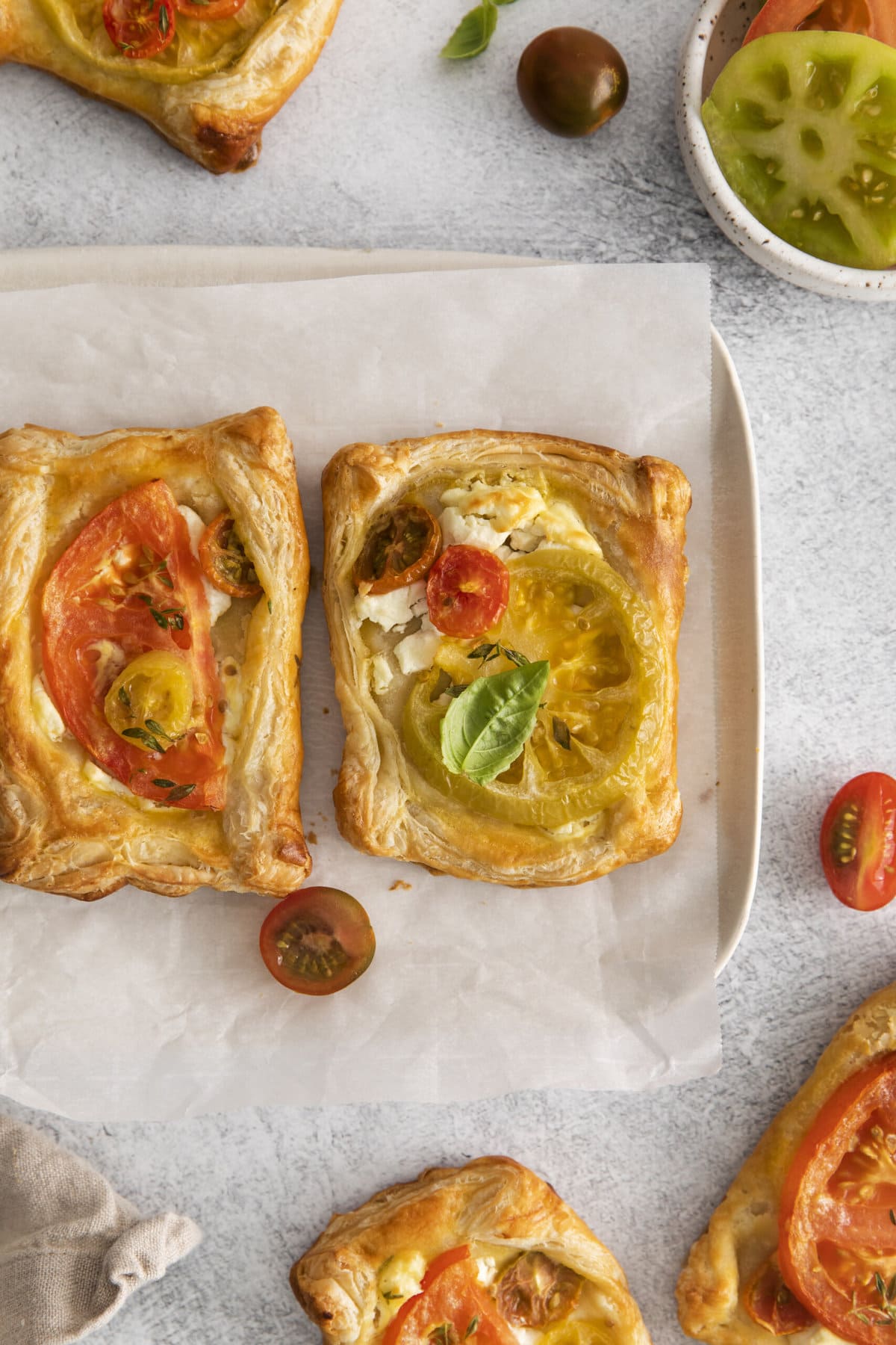 two tomato and goat cheese tarts on parchment paper with tomatoes around it.