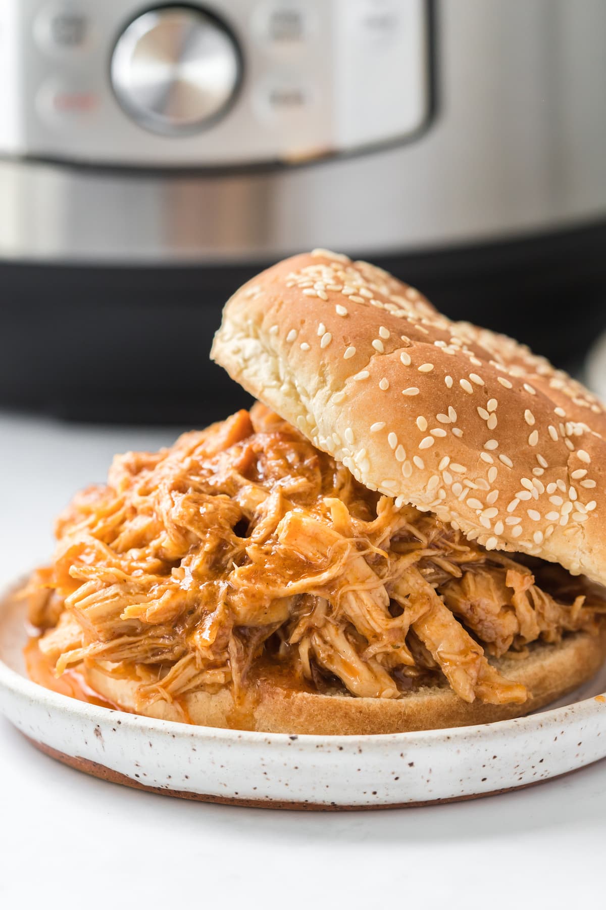 bbq shredded chicken in a sesame seed bun in front of an instant pot on a plate on a table