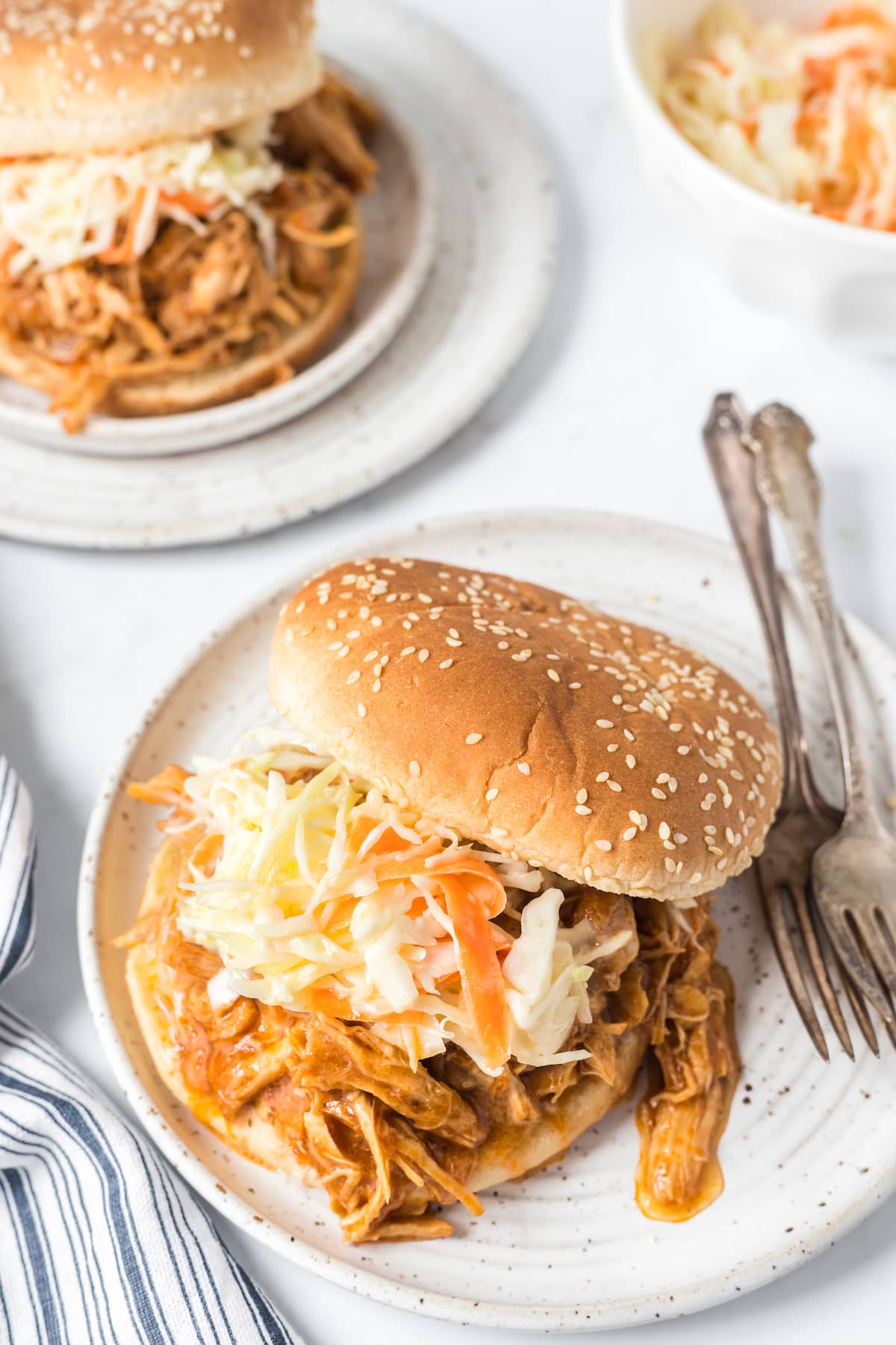 bbq shredded chicken coleslaw sandwich with bbq sauce in a sesame bun on a white plate in front of an instant pot