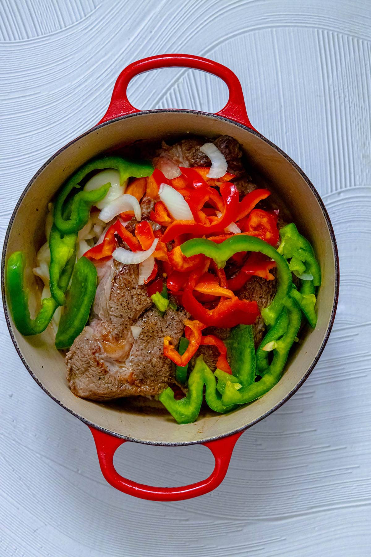 browned pot roast with sliced bell peppers and onions in a dutch oven