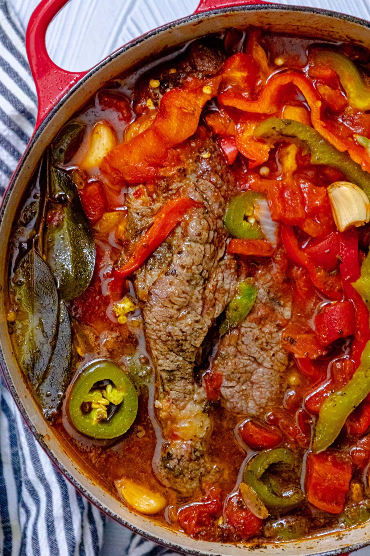 pot roast in a dutch oven with peppers, onions, bay leaves, garlic, and jus in a dutch oven 