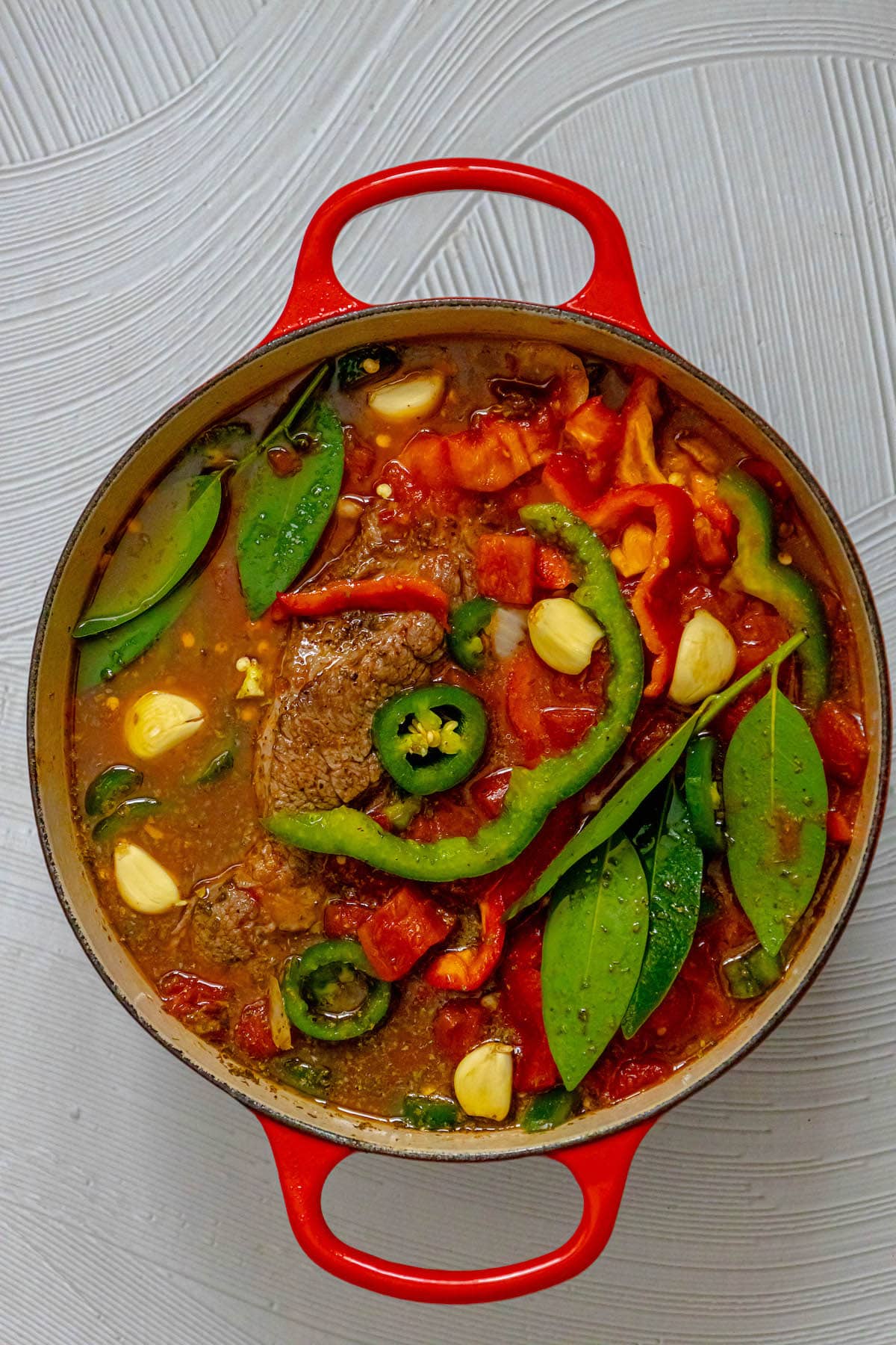 pot roast with sliced peppers and jalapeños with garlic and bay leaves in stock in a dutch oven