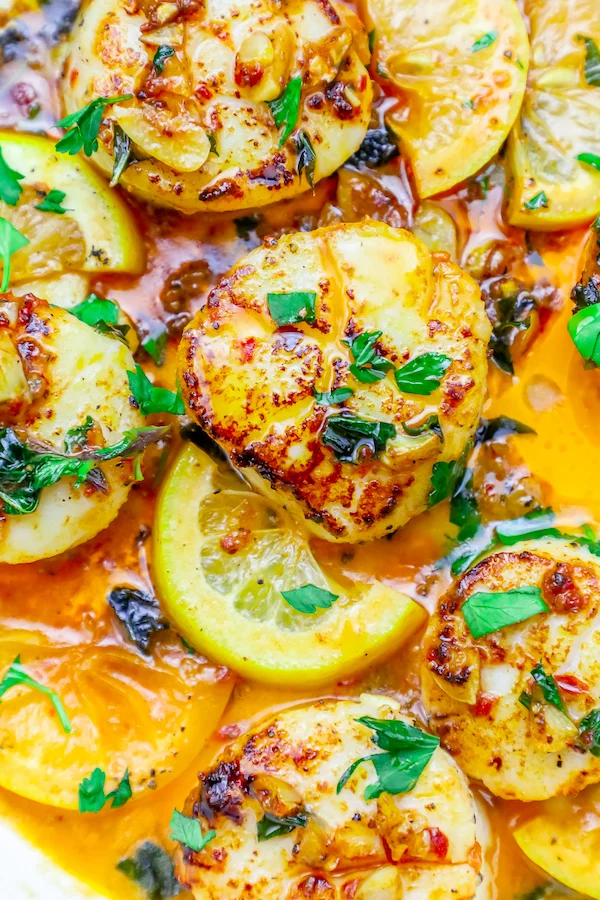 seared scallops in a pan with chopped cilantro and chili sauce on top next to slices of lemon