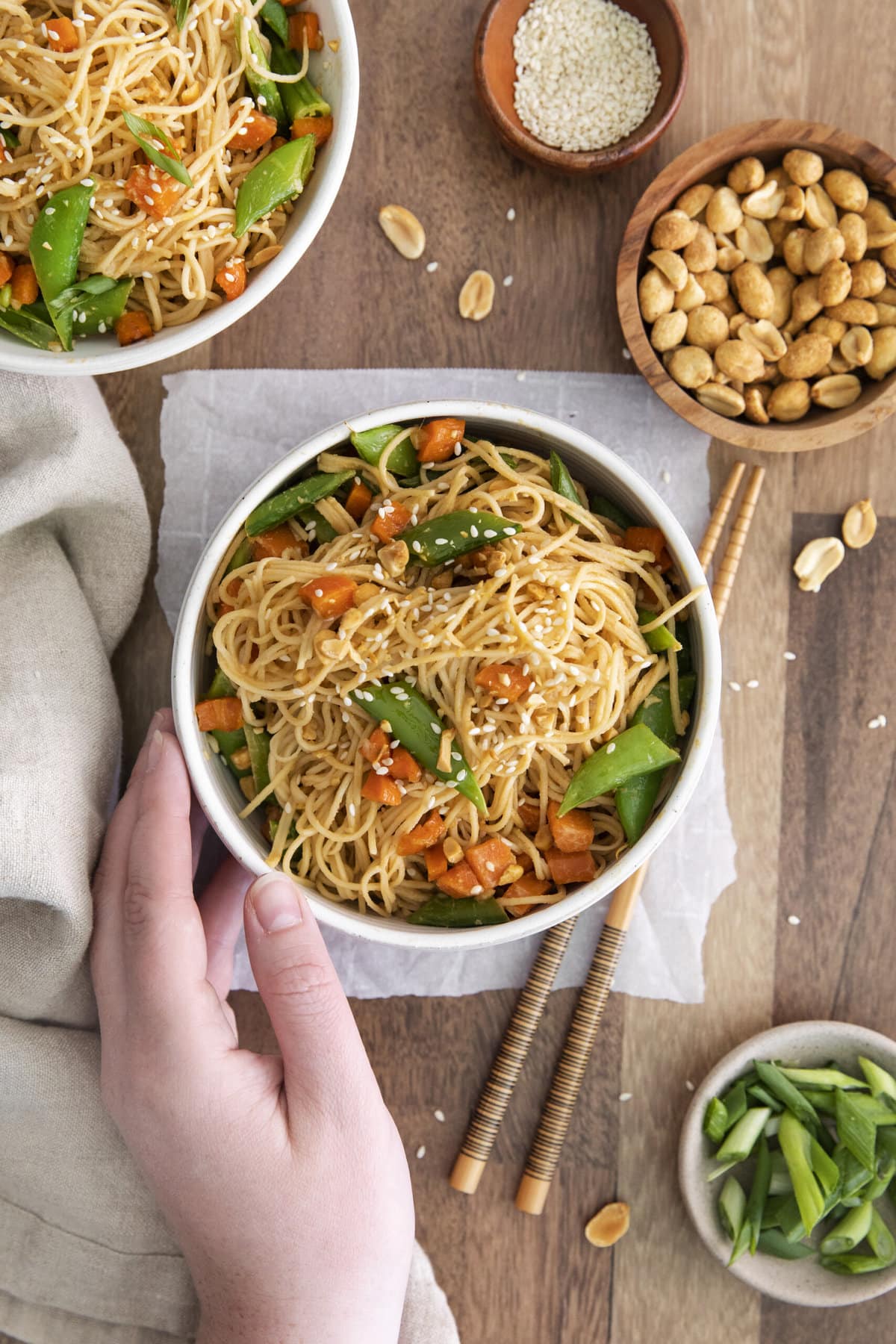 thai noodles with carrots, peas, and hand along the bowl.