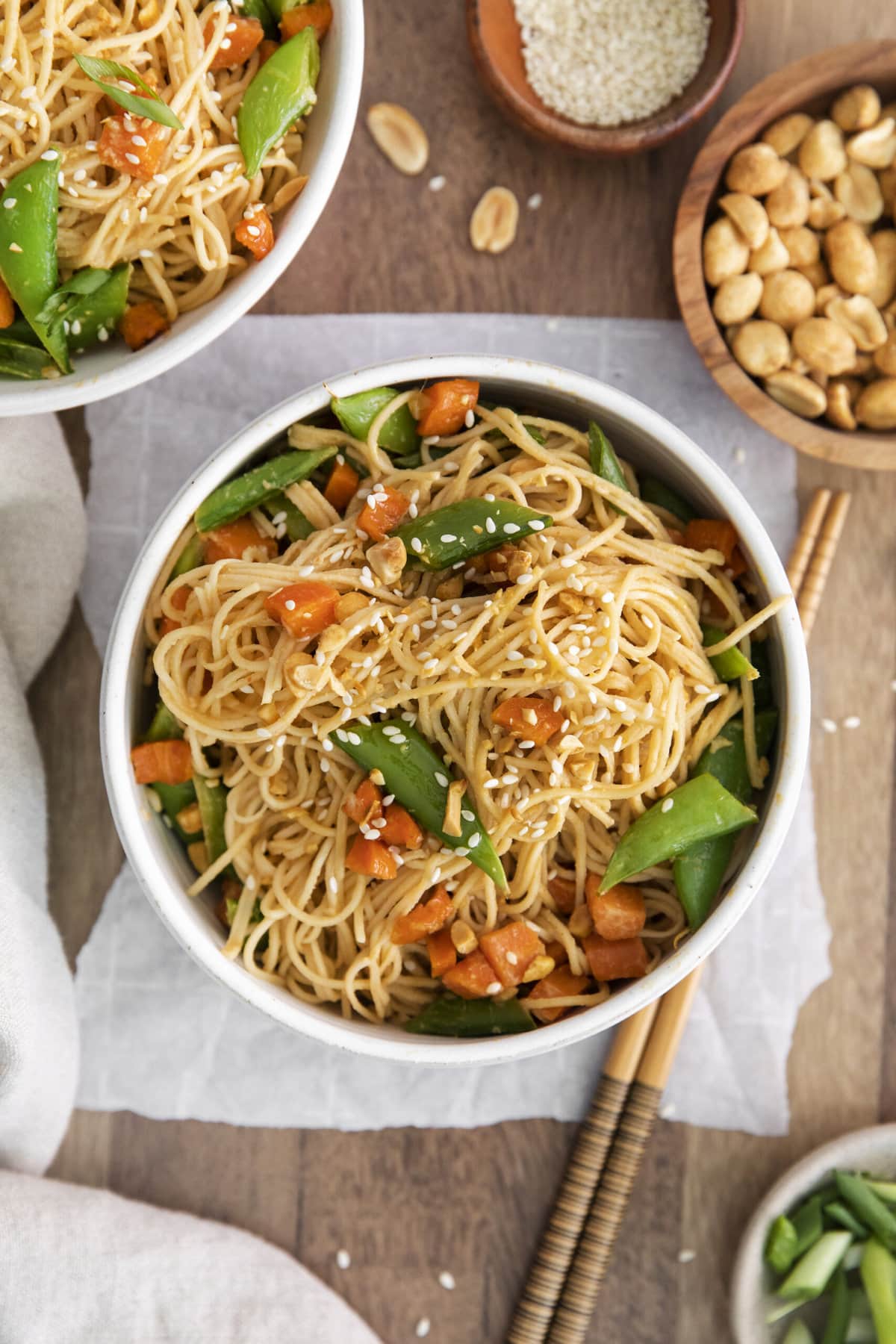 noodles tossed in peanut sause with sesame seeds, snap peas, carrots, chopped peanuts, and vegetables on a table with chopsticks