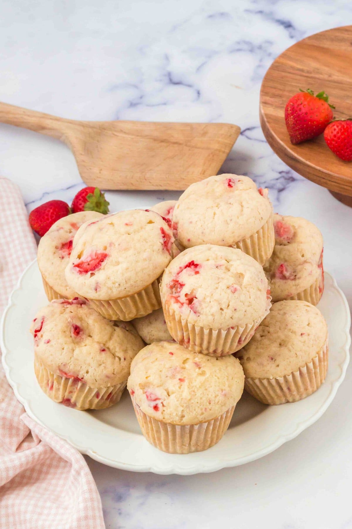 stack of strawberry muffins on a white plate with wooden spatula in background.