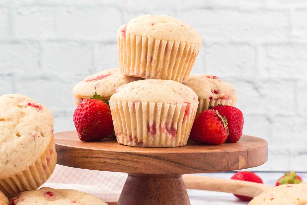 three strawberry muffins on a wooden cake stand.