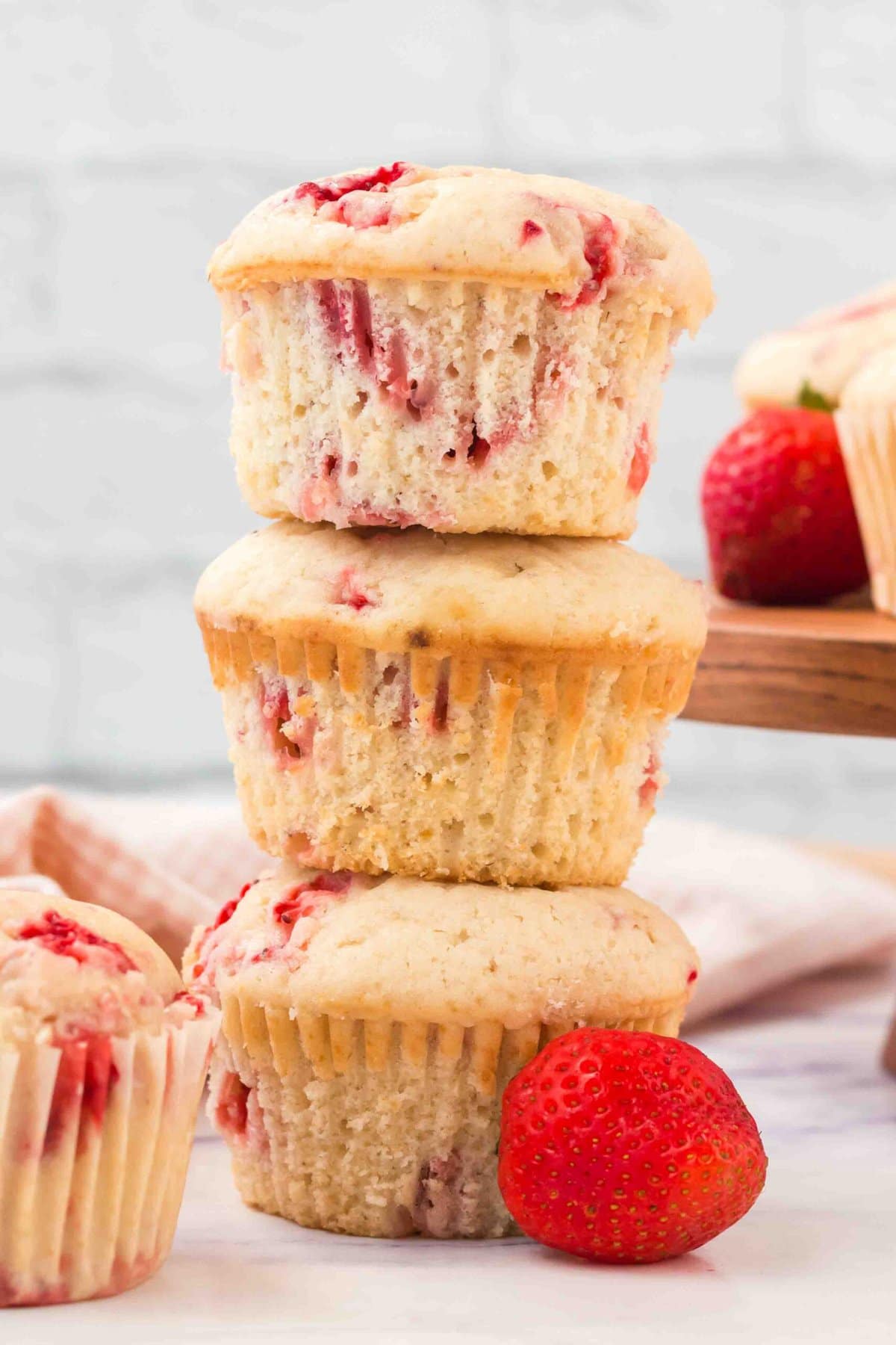 three strawberry muffins stacked, strawberry next to it. 