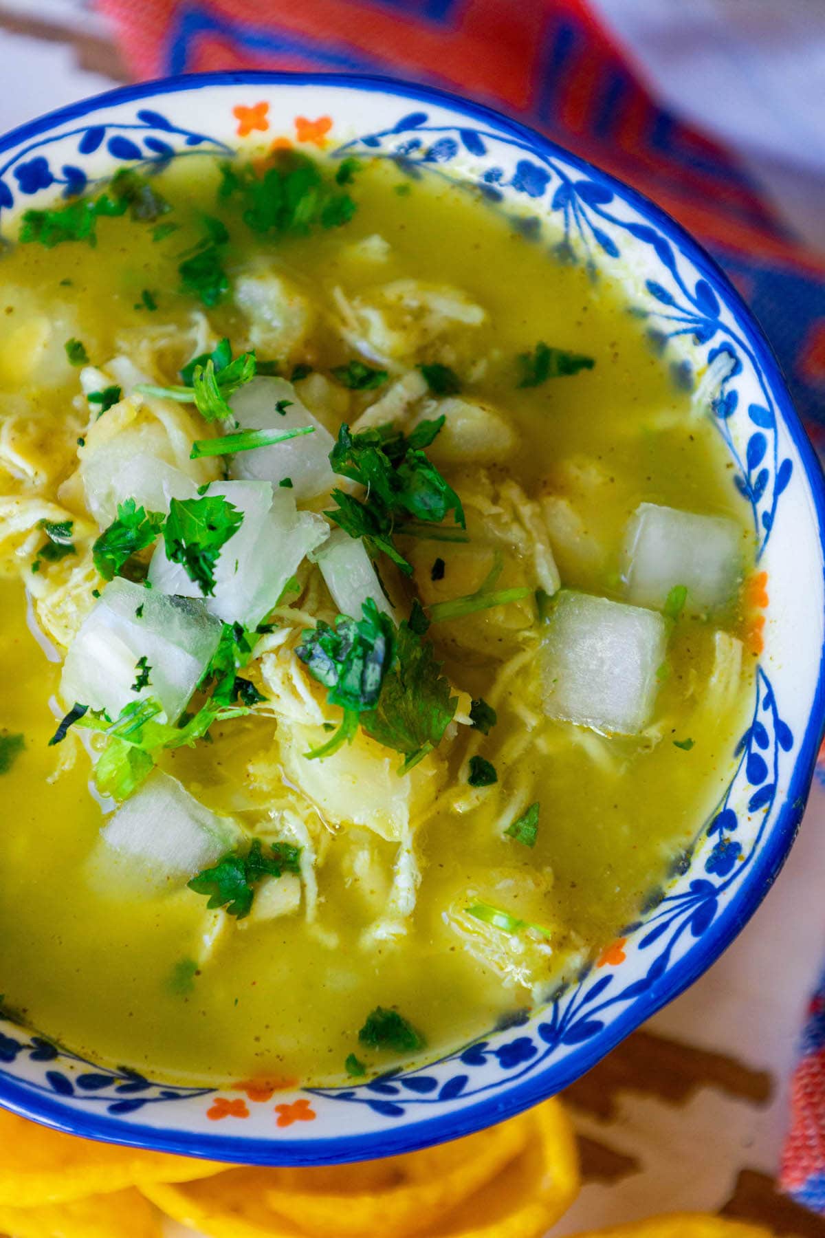 green posole chicken soup in a blue bowl with chopped onion and cilantro on top 