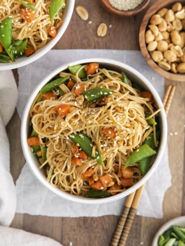 noodles tossed in peanut sause with sesame seeds, snap peas, carrots, chopped peanuts, and vegetables on a table with chopsticks