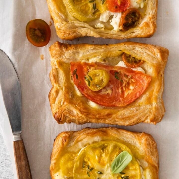 two tomato and goat cheese tarts on parchment paper with tomatoes around it.