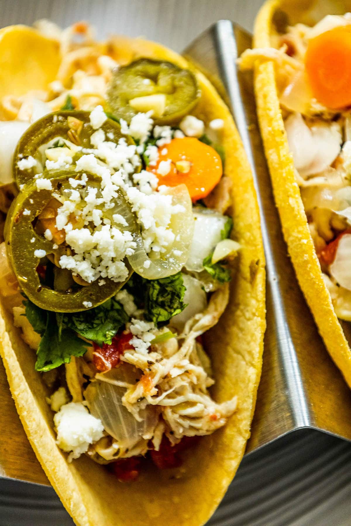 chicken tacos with shredded chicken, pickled jalapenos, crumbled white cheese, onions, chopped cilantro, diced onion, and pickled carrot in a metal stand