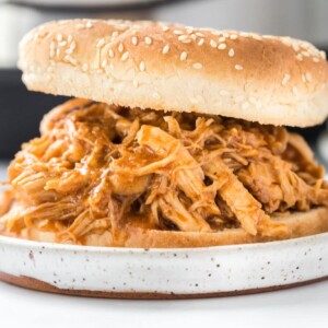 shredded chicken sandwich with bbq sauce in a sesame bun on a white plate in front of an instant pot