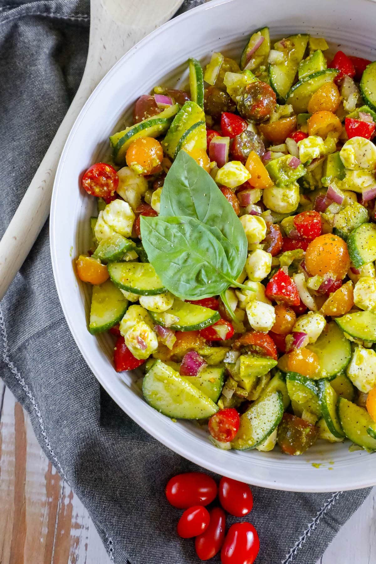 chopped cucumbers, cherry tomatoes, onion, crumbled feta cheese, and basil in a white bowl tossed in pesto sauce