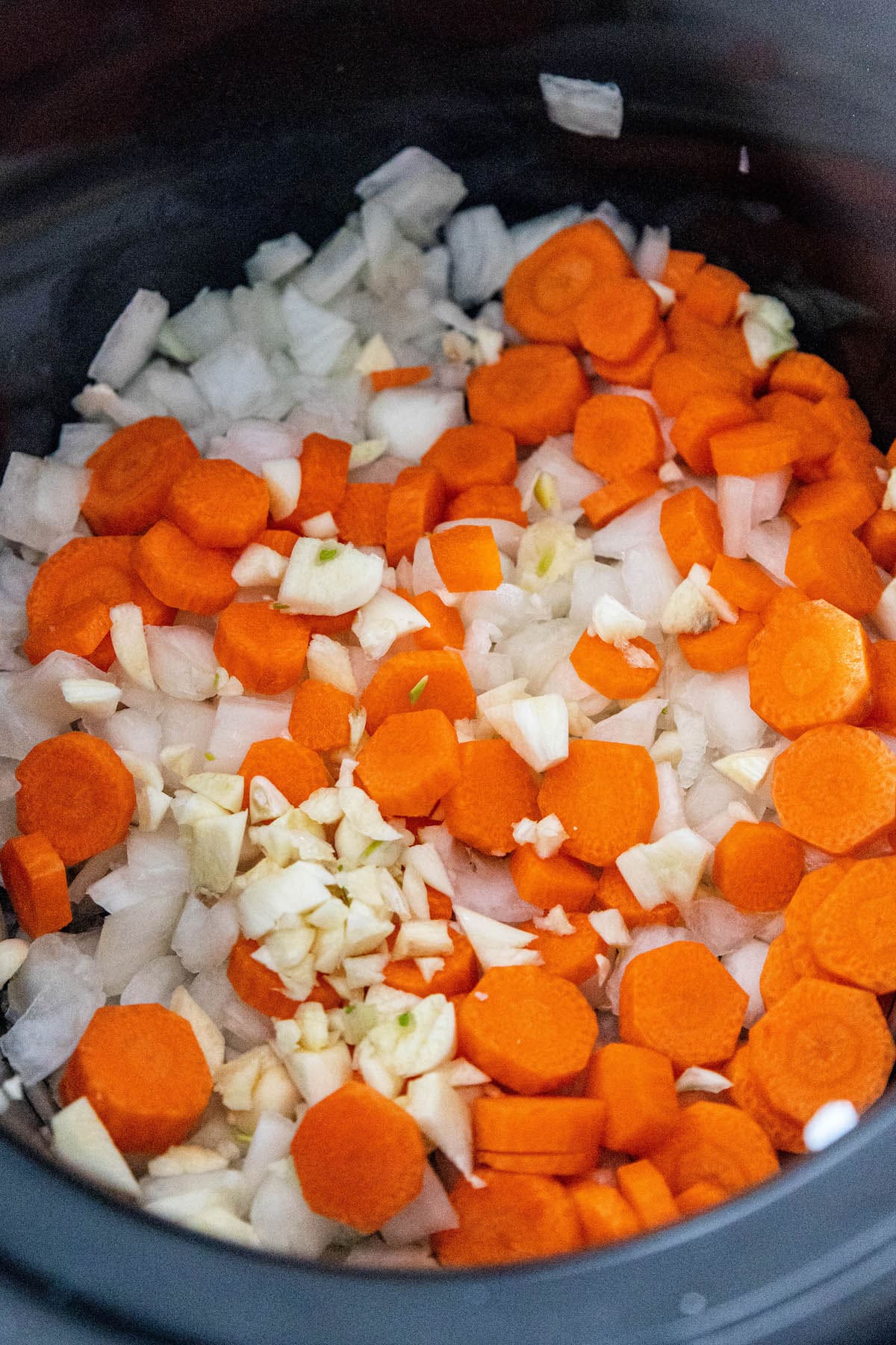 A slow cooker filled with carrots and onions, cooking Slow Cooker Chuck Roast Steak in Gravy.