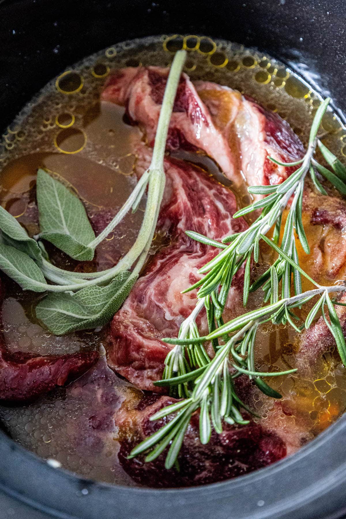 A slow cooker chuck roast steak in gravy with sprigs of sage.