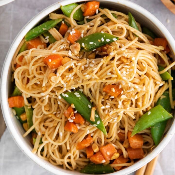 noodles with carrots, peas, peanuts, and chopsticks along the bowl.