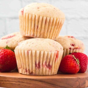strawberry muffins stacked on top of each other with strawberries on a wood platter