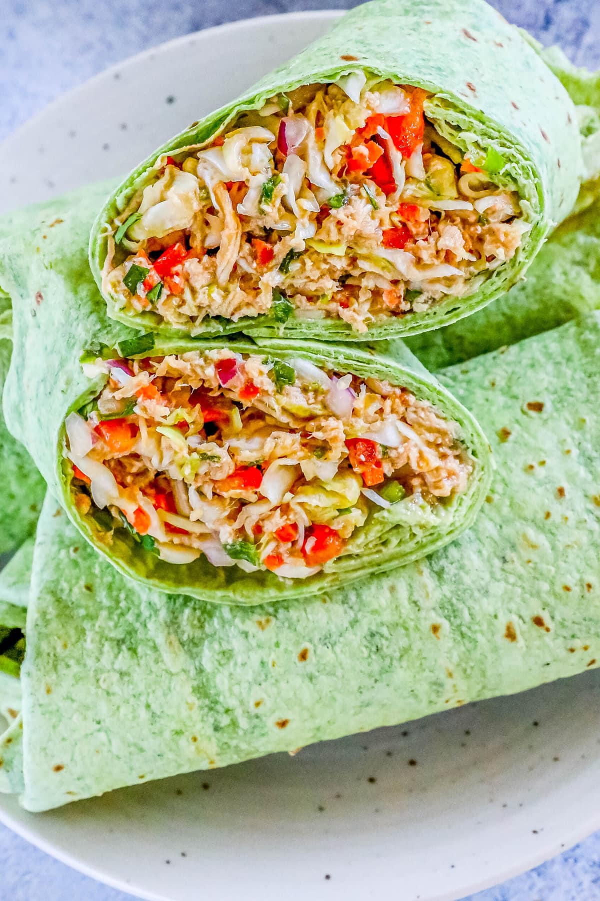 chicken salad with shredded chicken, cabbage, and diced vegetables wrapped in a green tortilla sliced in half on a white plate
