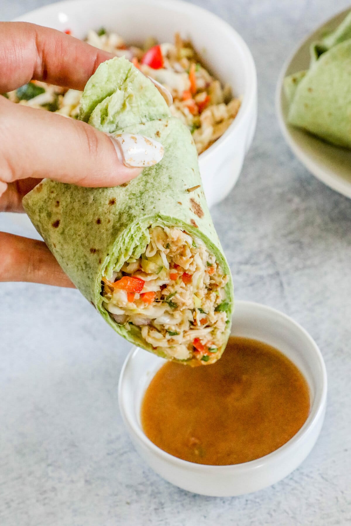 green spinach tortilla wrapped chicken salad sandwich being dipped into a cup of peanut sauce