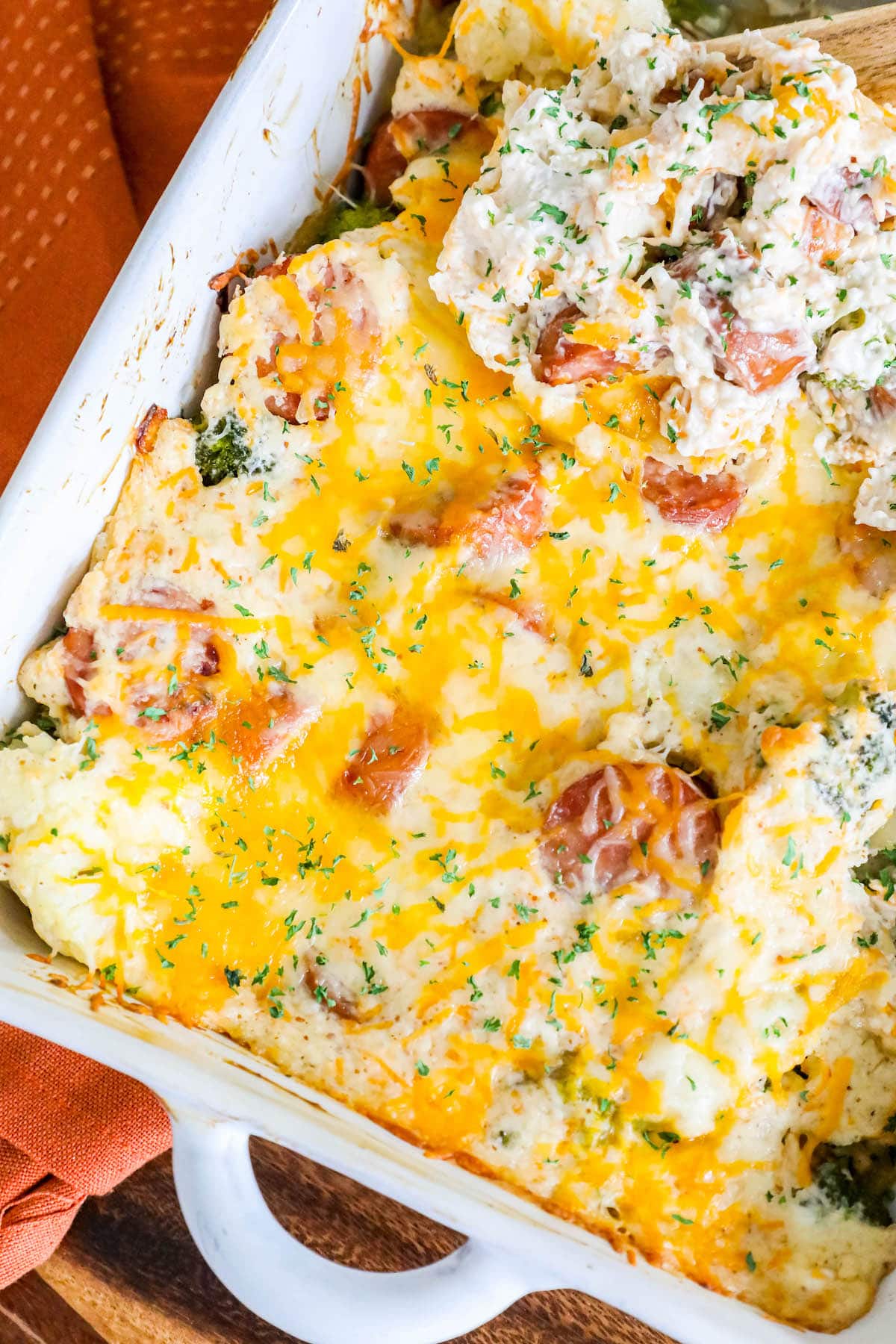 casserole with sliced sausage, broccoli, cauliflower, and herb seasonings topped with melted cheese in a white casserole dish on a table