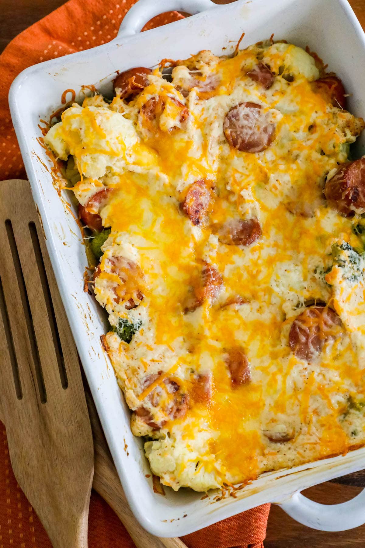 cheesy baked casserole with sliced sausage, broccoli, cauliflower, and herb seasonings in a white casserole dish on a table