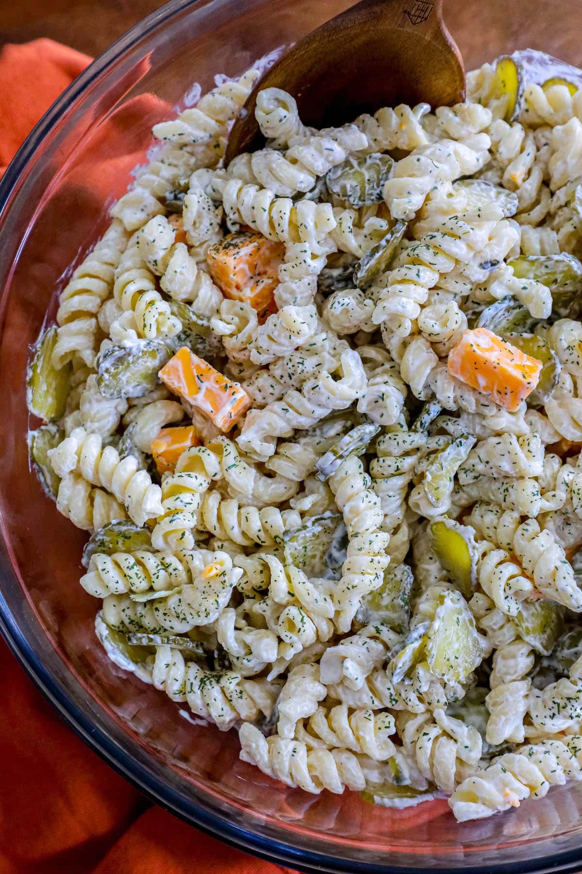 pasta salad mixed with chopped pickles and cheese tossed in dill mayonnaise sour cream dressing in a glass bowl 