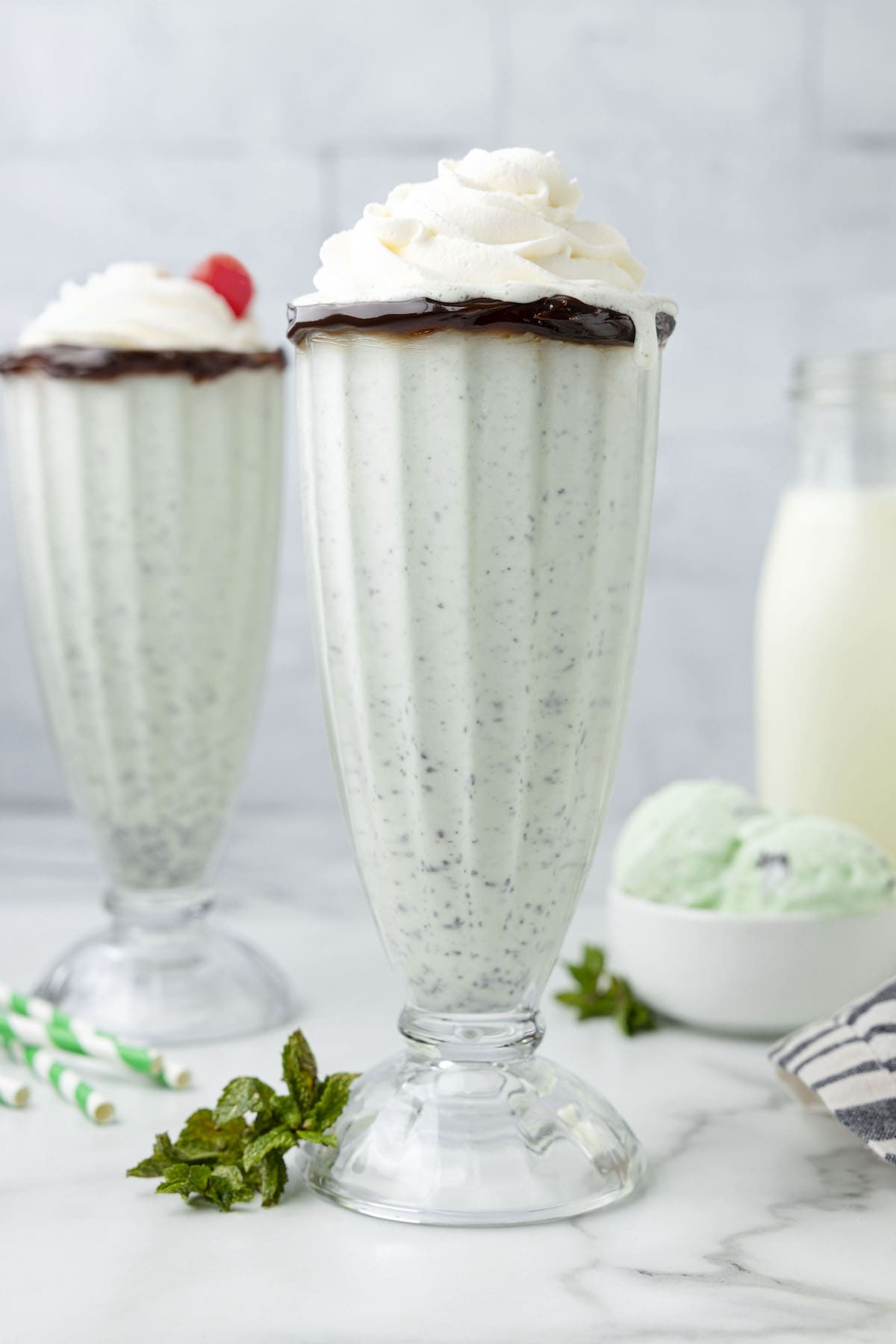 mint milkshake in a tall glass cup with whipped cream on top dripping down the side