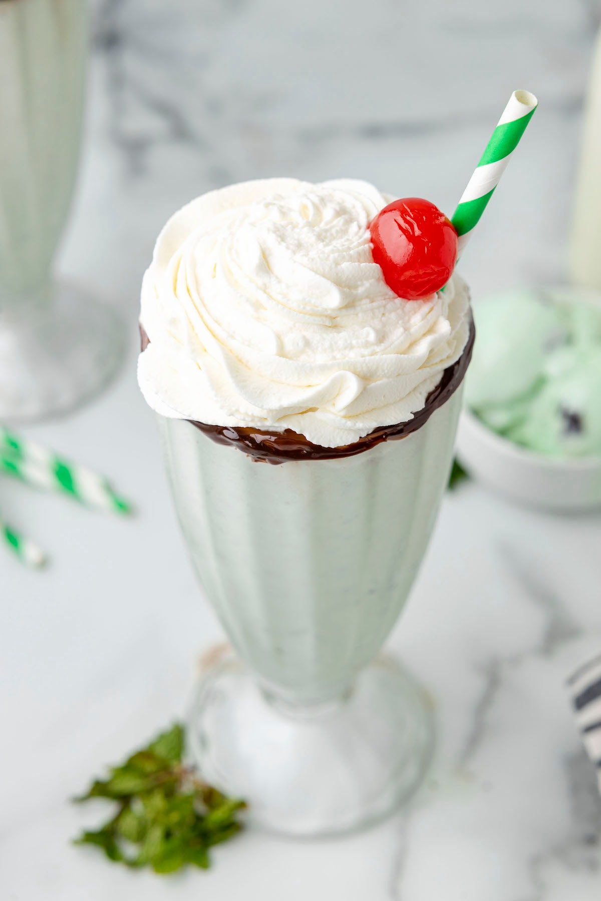 mint milkshake in a tall glass cup with whipped cream and a cherry on top, and a straw on the side