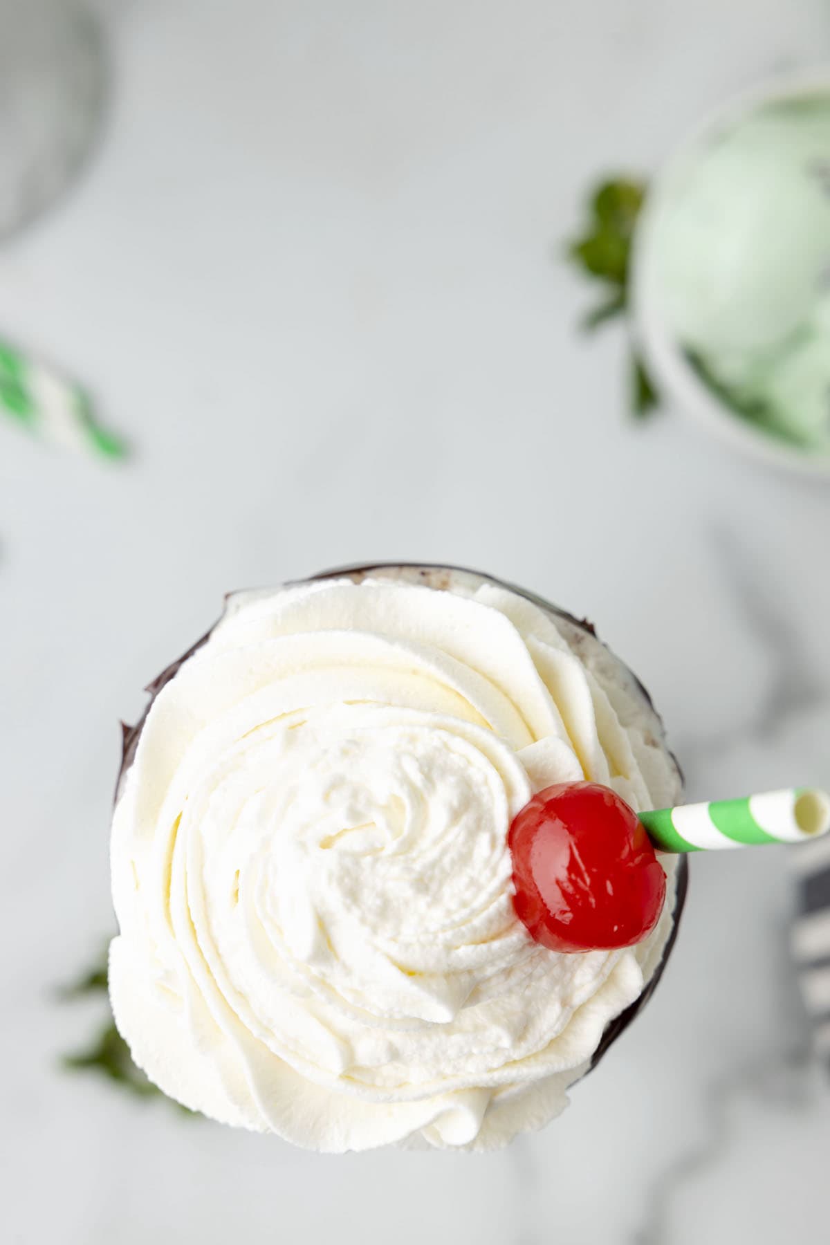 mint milkshake in a glass with lots of whipped cream on top and a cherry in the middle