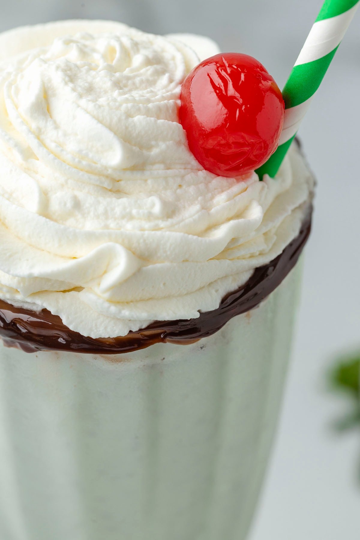 mint milkshake in a tall glass cup with whipped cream and a cherry on top, and a straw on the side