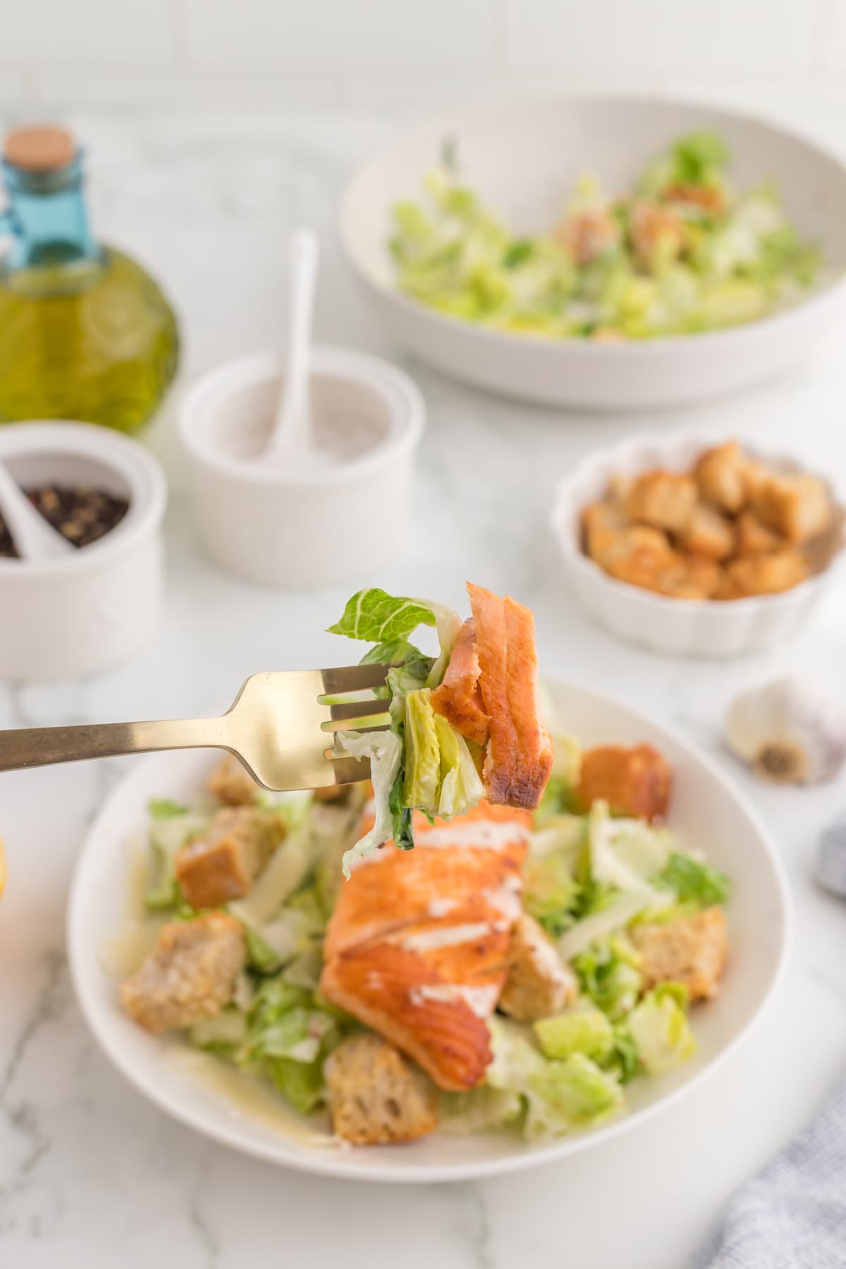 caesar salad with croutons in a white plate with a filet of salmon on top