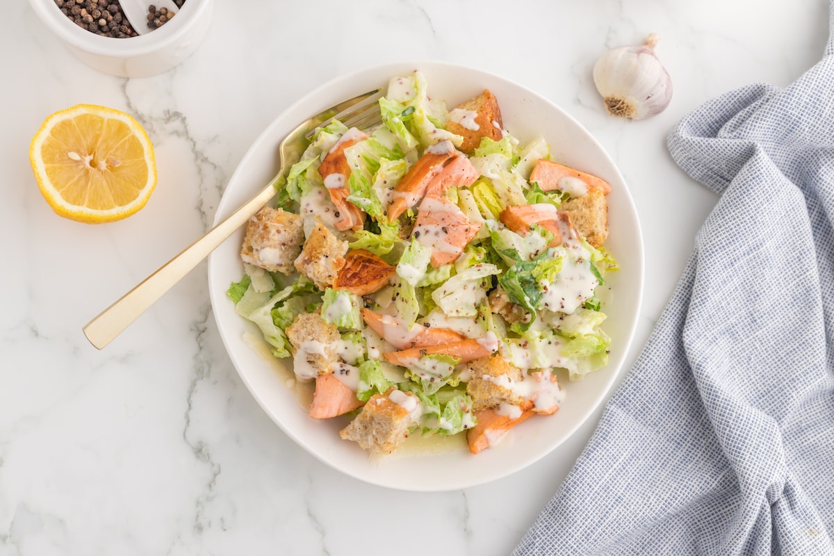 pieces of salmon filet over a salad with croutons and caesar dressing