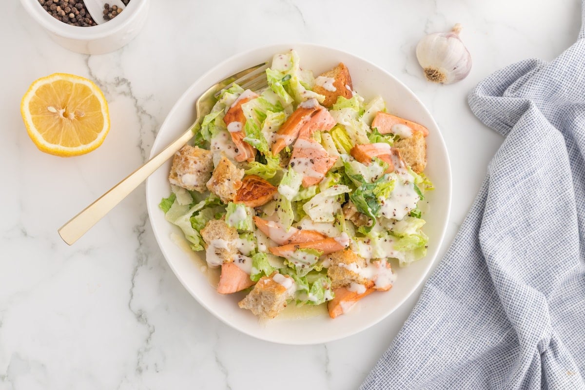 pieces of salmon filet over a salad with croutons and caesar dressing